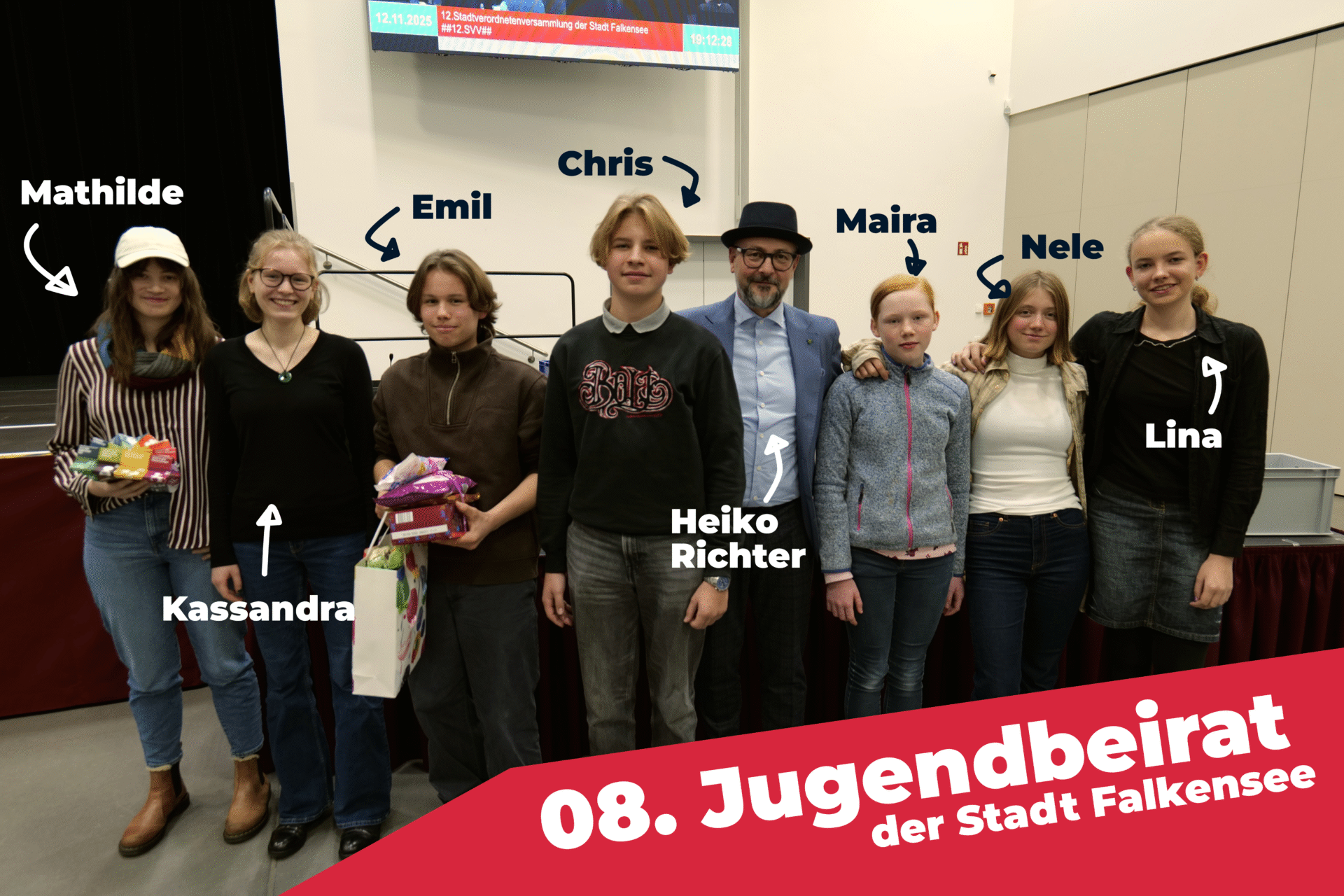 Gruppenfoto des 8. Jugendbeirats der Stadt Falkensee mit sechs Jugendlichen und dem Moderator Heiko Richter. Die Jugendlichen halten Geschenke in den Händen und stehen auf einer Bühne, während im Hintergrund eine Präsentation sichtbar ist.