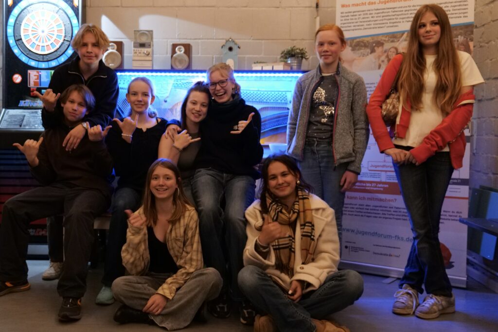 Gruppenszene von Jugendlichen in einem Jugendzentrum, lächelnd und in entspannter Pose, mit einer Dartscheibe im Hintergrund.